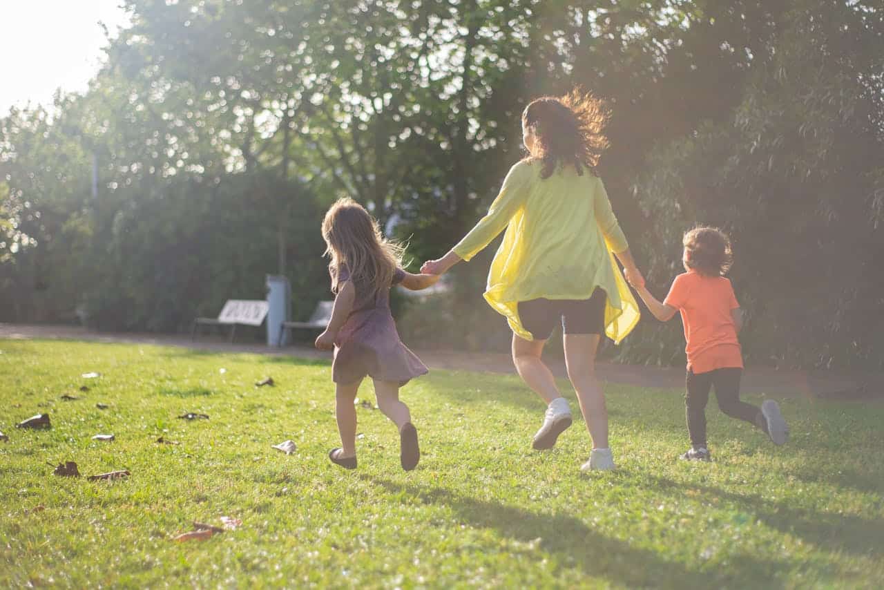A mother with two children running and playing in a sunny park, enjoying family time.