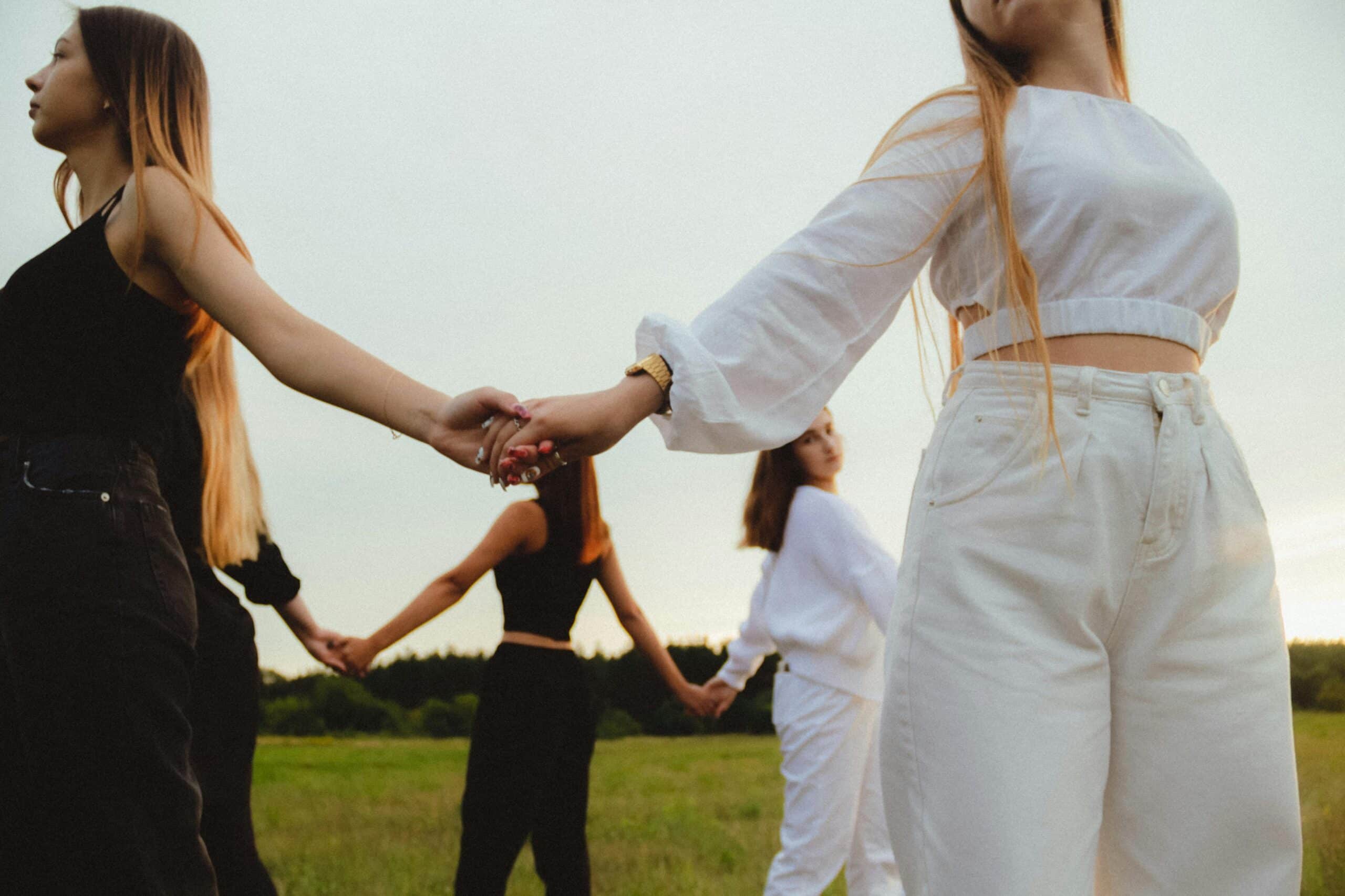 Group of young women holding hands in a sunny outdoor field, promoting unity and friendship.